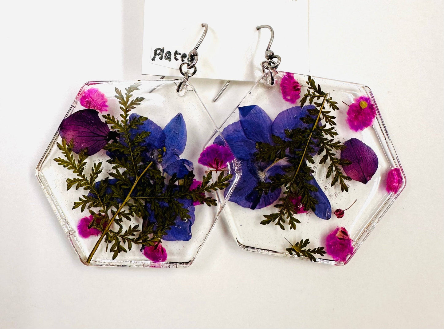 Hexagon resin earrings with purple and pink flowers and silver hooks. Bold pressed flower earrings with a geometric shape.