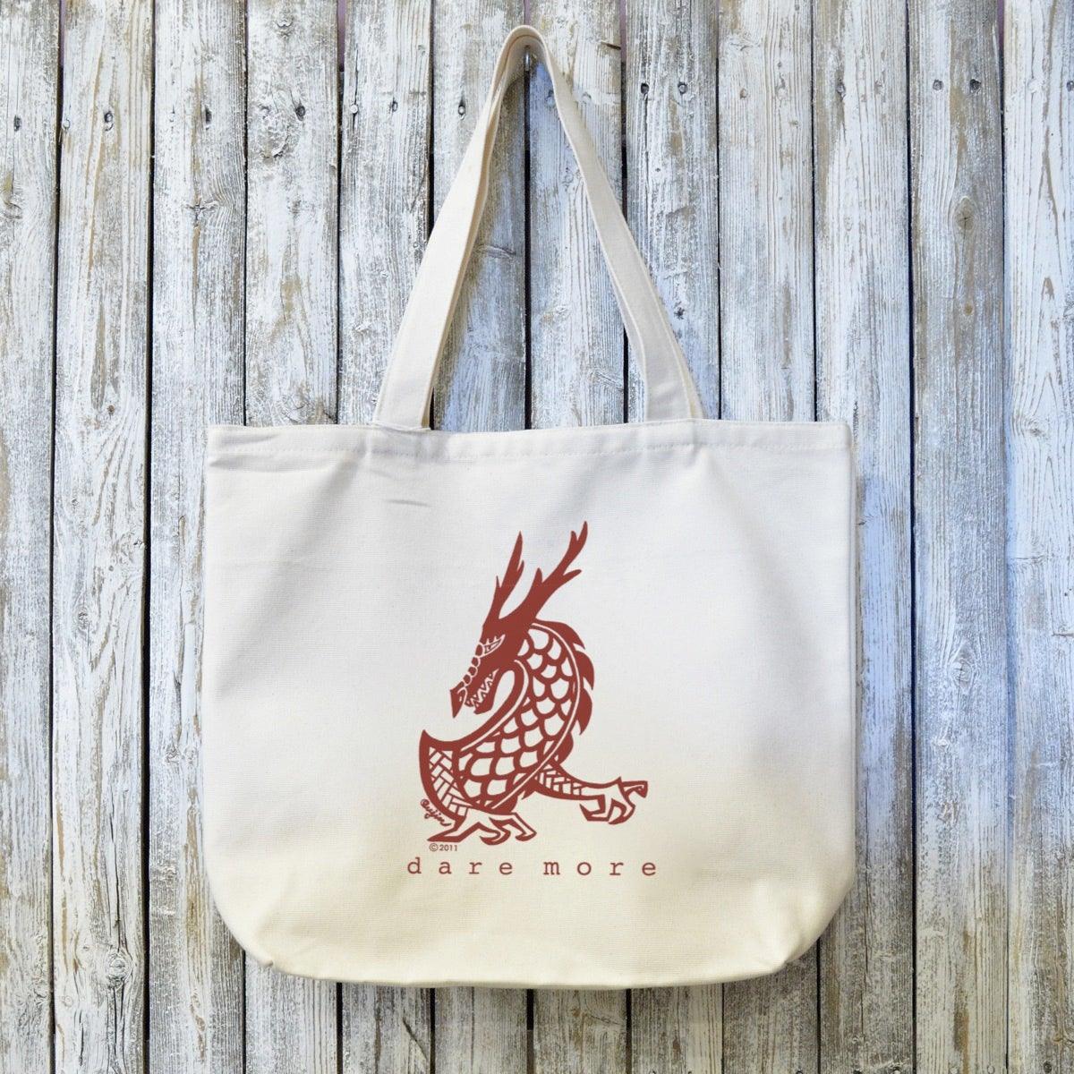 Dragon Gift Tote Bag - Organic Canvas with bold red dragon design and 'dare more' text. Eco-friendly and artist-designed for sustainable style.