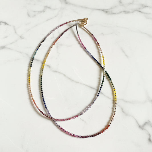 Colorful gemstone rainbow necklace with seed beads on white marble surface