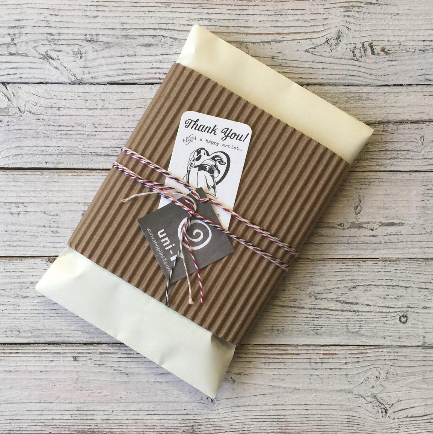 Eco-conscious gift packaging for Uni-T kids' 'Dance More' t-shirt, wrapped with kraft paper, string, and thank-you tag.