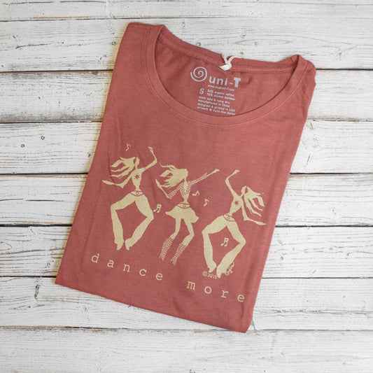 Women's Dance T-Shirt in Bamboo & Organic Cotton in rose color with 'Dance More' dancer graphic folded on wood background. Ideal gift for dancers.