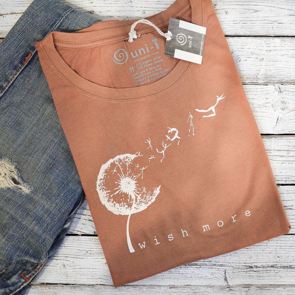 Folded Women's Dandelion T-Shirt in rust color with 'Wish More' design, made from bamboo & organic cotton. Eco-friendly inspirational gift tee.
