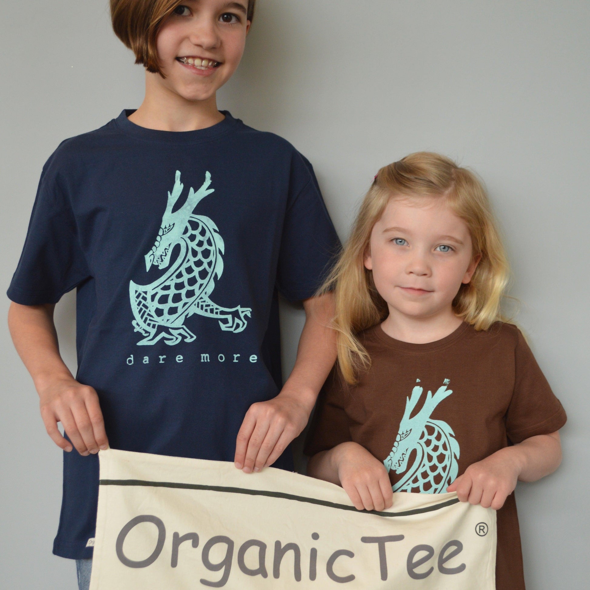 Kids wearing Uni-T 'Dare More' dragon graphic T-shirts in navy and brown, made from organic cotton. Eco-friendly fantasy apparel for children.