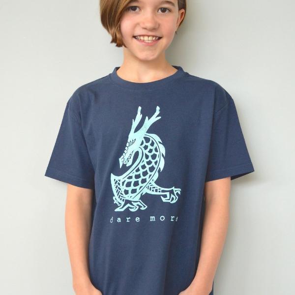 Child modeling navy Uni-T Kids' Organic Cotton T-Shirt with light blue dragon and 'dare more' slogan. Eco-friendly fantasy apparel.