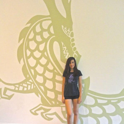 Model posing in front of a large dragon mural while wearing the 'Dare More' bamboo-organic cotton T-shirt. Eco-friendly mythical creature tee by Uni-T.