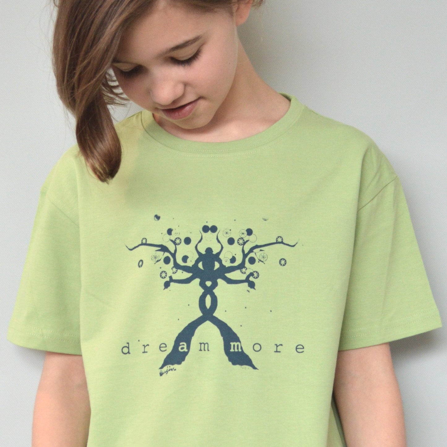 Child wearing green Kids' Organic Cotton T-Shirt with blue 'Dream More' graphic. Eco-friendly inspirational top by Uni-T for children.