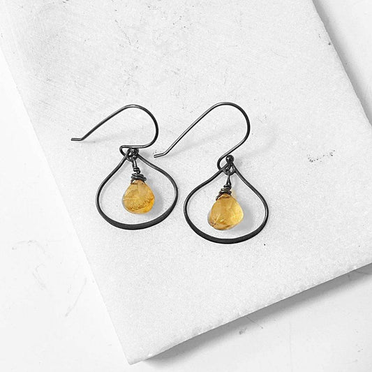 Citrine silver hoop earrings with teardrop citrine gemstones wrapped in oxidized silver wire, displayed on a white stone background.