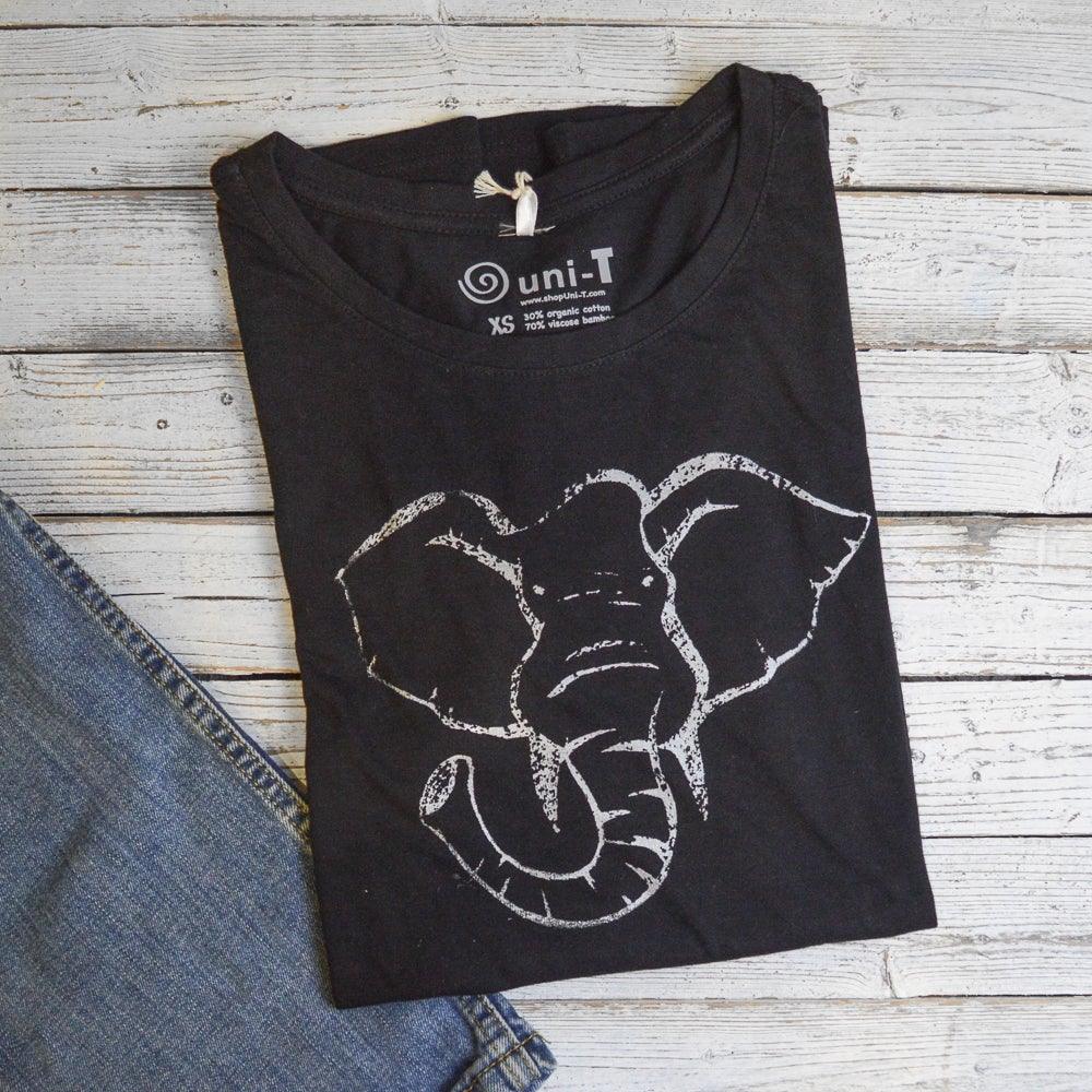 Black Women's Elephant T-Shirt in bamboo & organic cotton with white elephant print, folded next to denim jeans. Sustainable wildlife graphic tee.