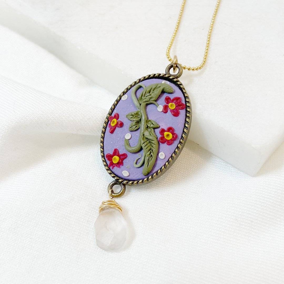 Detailed view of Uni-T Polymer Clay Floral Necklace with red floral accents and green leaves on lavender pendant, finished with a clear teardrop bead.