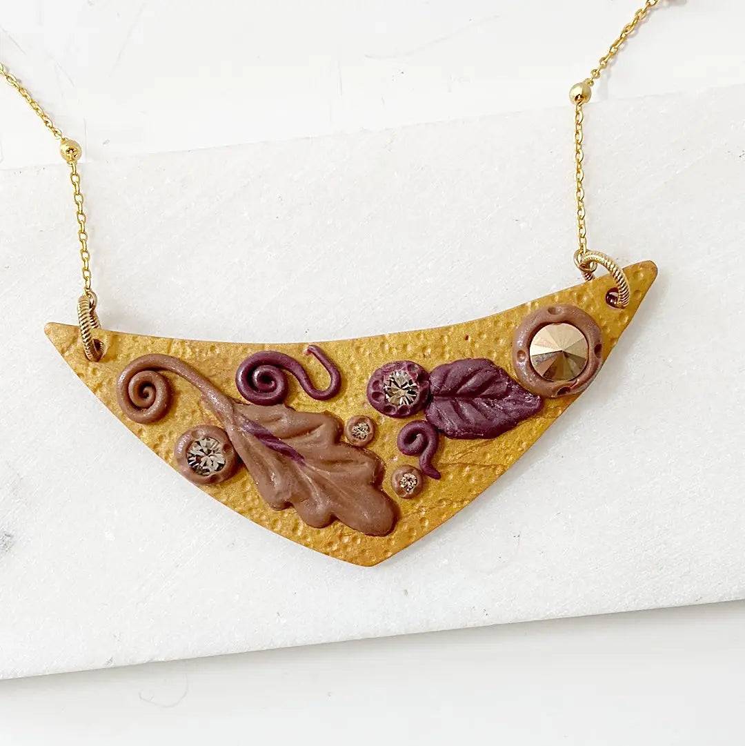 Fall Leaves Bib Necklace with polymer clay pendant featuring autumn leaf designs, crystals, and gold-plated chain. Unique statement jewelry piece.
