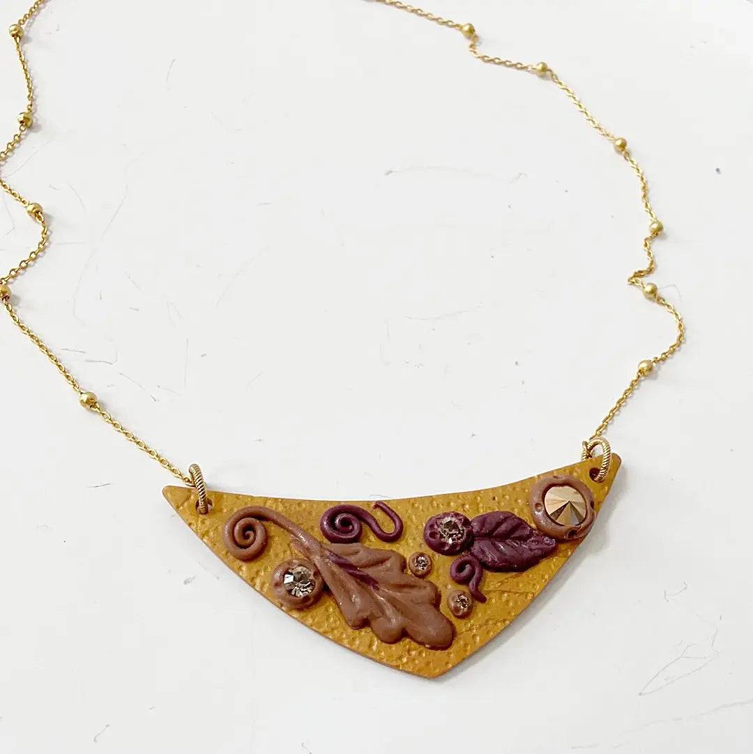 Handcrafted Fall Leaves Bib Necklace with textured polymer clay pendant, gold chain, and crystal accents. Ideal for seasonal or gift wear.