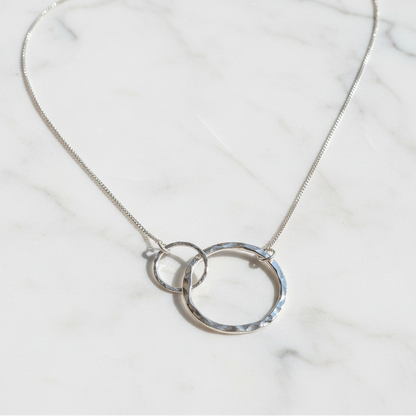 Silver necklace with interlocking rings on a textured surface