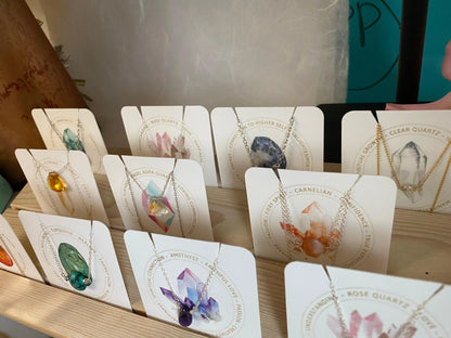 Assorted birthstone necklaces on display cards, showcasing handcrafted crystal pendants like rose quartz, carnelian, and clear quartz.