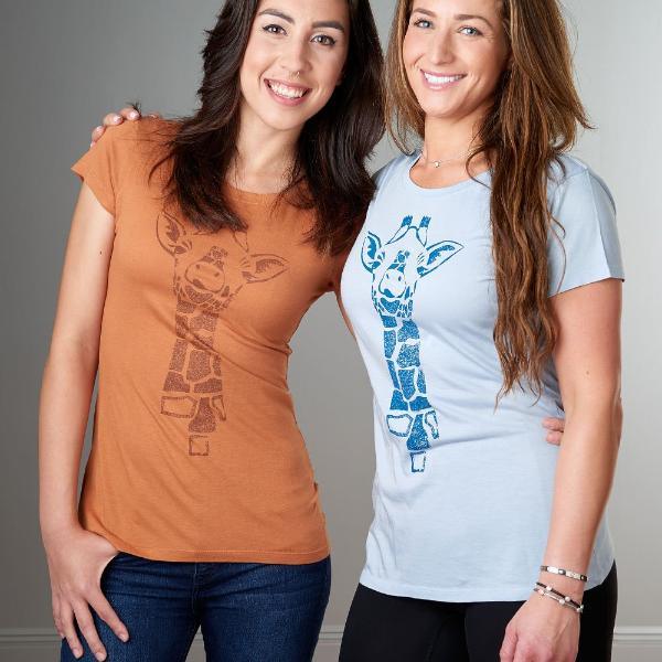 Two women wearing Uni-T giraffe graphic T-shirts in rust and light blue. Eco-friendly bamboo and organic cotton safari-style tops for women.