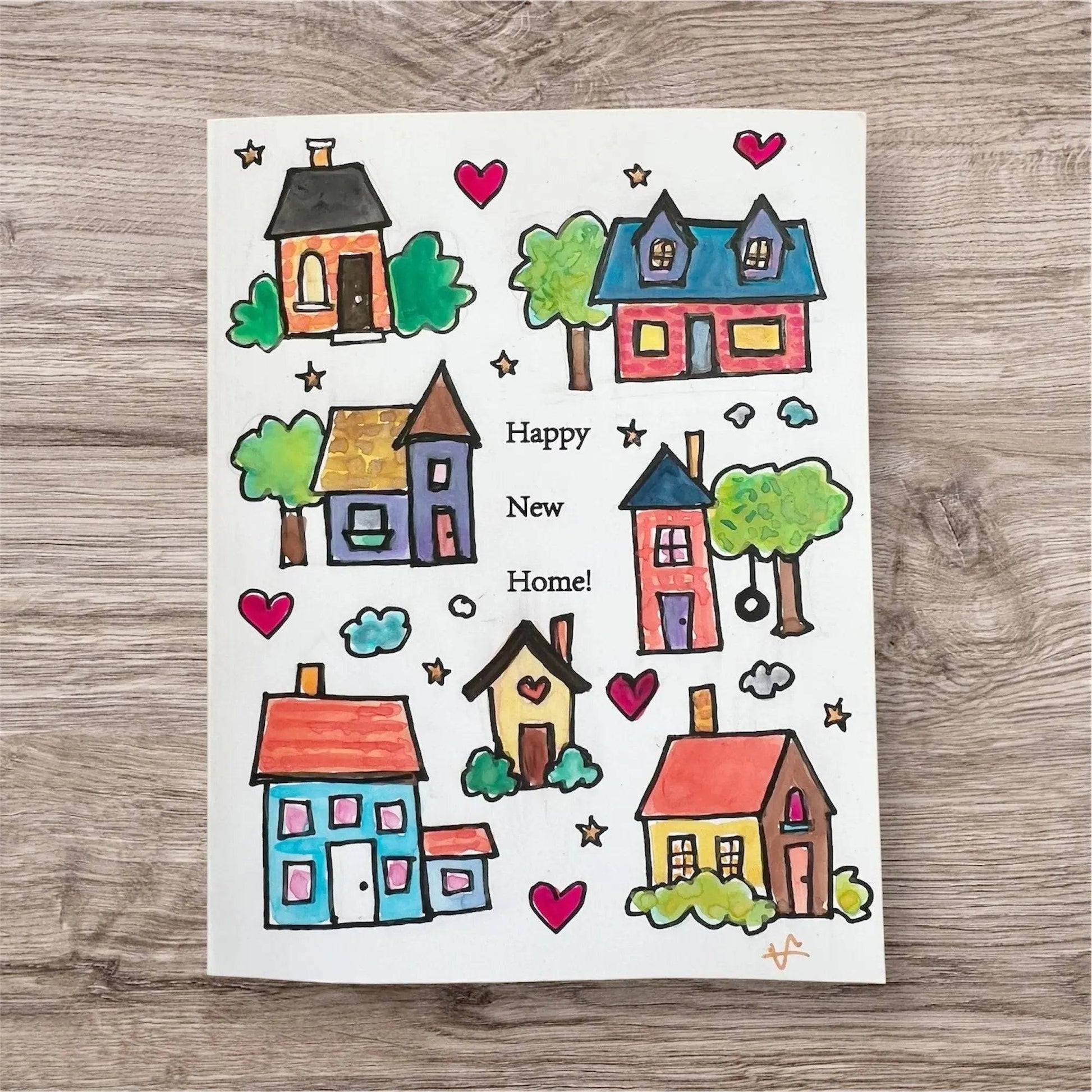 Happy New Home card from Good Vibe Tribe collection featuring colorful hand-painted houses, hearts, and stars on a white background. Handmade inspirational greeting card perfect for celebrating a new home.