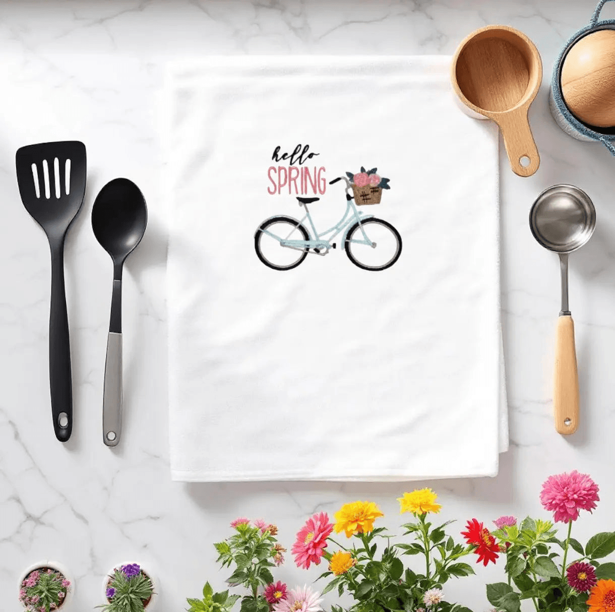 Hello Spring Bike Towel featuring an embroidered blue bicycle with a flower basket, styled on a kitchen counter with utensils and spring flowers.