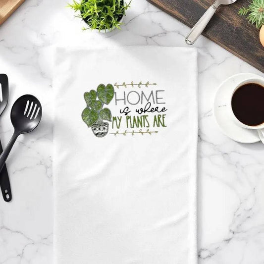 Embroidered plant towel on marble kitchen counter with utensils and coffee, featuring 'Home is where my plants are' design. Ideal for home decor gifts.