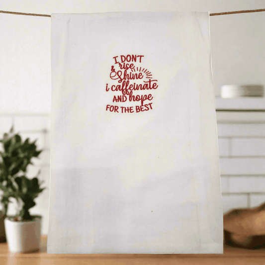 White embroidered kitchen towel hanging with red coffee-themed quote, perfect small gift for morning routines and caffeine enthusiasts.