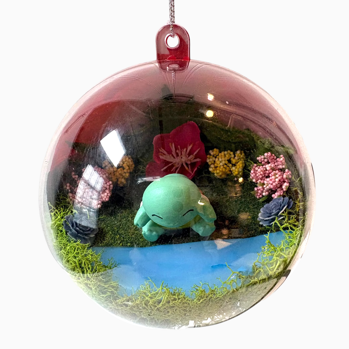 Uni-T Pokeball terrarium ornament featuring a miniature Squirtle figure in a mossy landscape with faux flowers