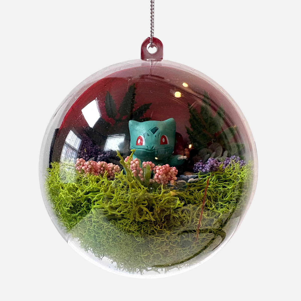 Uni-T Pokeball terrarium ornament featuring a Bulbasaur figure surrounded by green moss and pink flowers