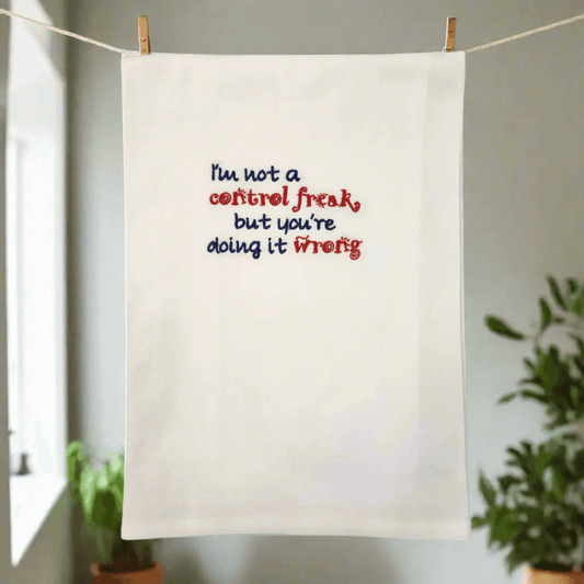 Unique gift idea towel hanging on a line, featuring humorous embroidered phrase in red and blue. Ideal for kitchen decor or gifting.