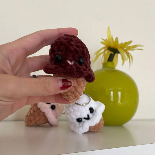 Hand holding a handmade Ice Cream Cone Keychain made of soft chenille yarn in chocolate color. Plush accessory with safety eyes, ideal for small gifts.