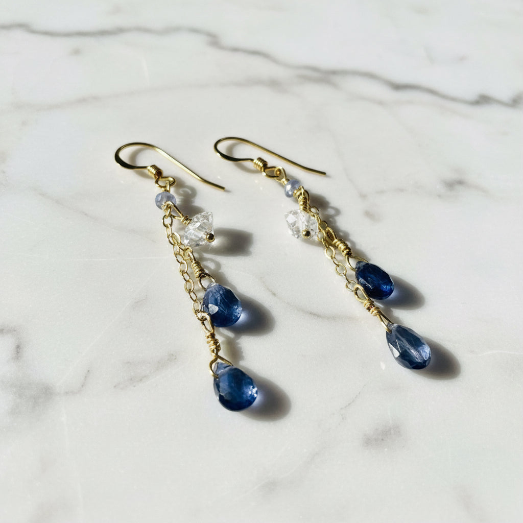 Gold chain drop earrings with blue and clear gemstones on white background