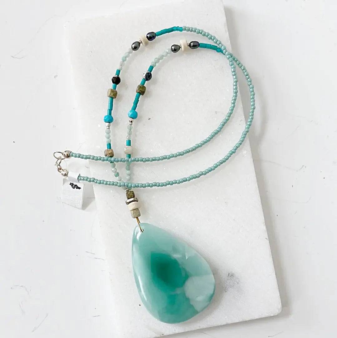 Dark green moonstone necklace with iridescent teardrop pendant, turquoise beads, and sterling silver clasp, displayed on white background.