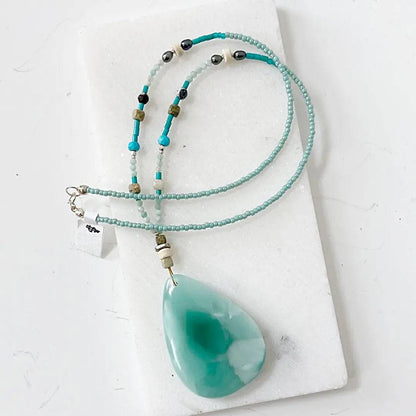 Dark green moonstone necklace with iridescent teardrop pendant, turquoise beads, and sterling silver clasp, displayed on white background.