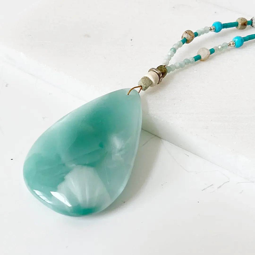 Close-up of iridescent dark green moonstone teardrop pendant with turquoise and sterling silver beadwork on necklace chain.