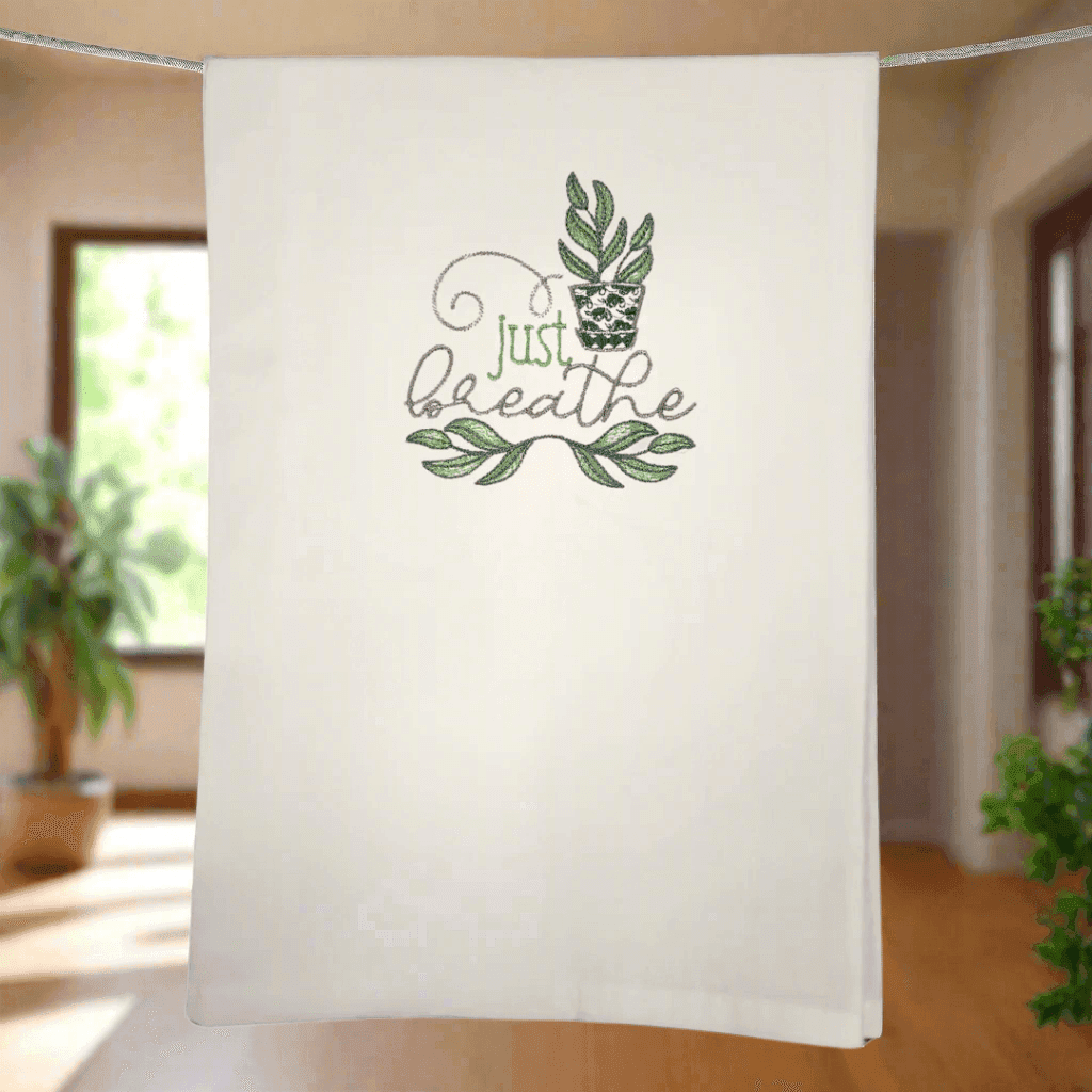 Just Breathe plant towel - embroidered with leafy design, hanging in sunlit kitchen. Stylish and functional kitchen towel for home decor.