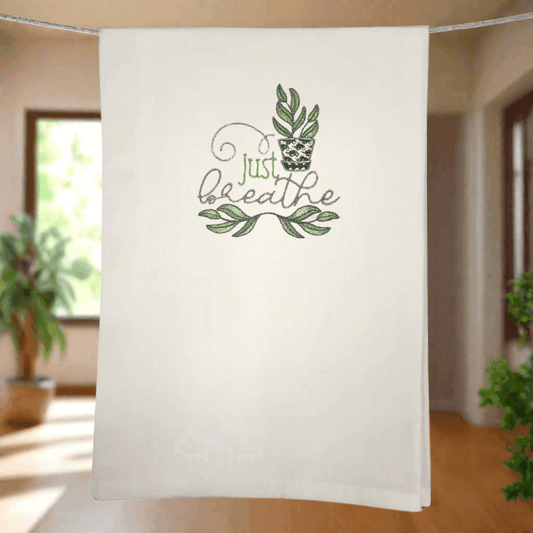 Just Breathe plant towel - embroidered with leafy design, hanging in sunlit kitchen. Stylish and functional kitchen towel for home decor.