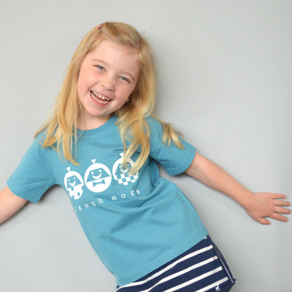 Smiling child wearing Kids' Happy Vibe Organic Cotton T-Shirt in teal blue with 'Laugh More' graphic. Eco-friendly playful shirt for children.