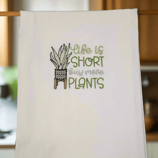 Hanging embroidered kitchen towel featuring 'Life is Short Buy More Plants' design, ideal for cozy indoor garden-themed kitchens.
