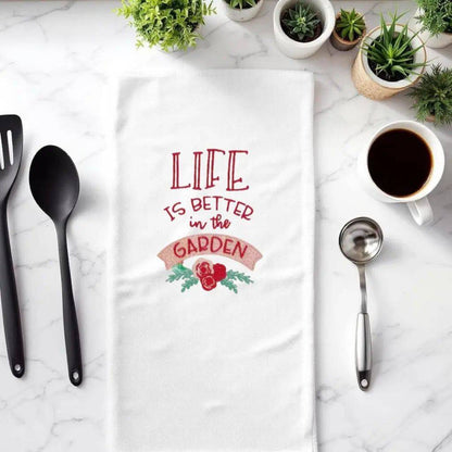 Garden embroidered towel with 'Life is Better in the Garden' text, styled on a kitchen counter with utensils and coffee. Ideal kitchen charm gift.