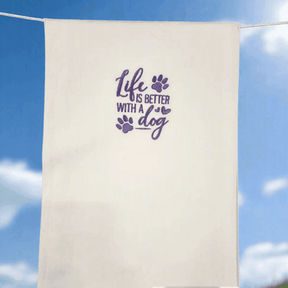 Dog Embroidered Towel with 'Life is Better with a Dog' message in purple, hanging outdoors against a blue sky background.