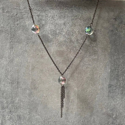 Elegant long crystal chain necklace with multicolor beads and tassel detail, shown on a gray textured display for layering jewelry.