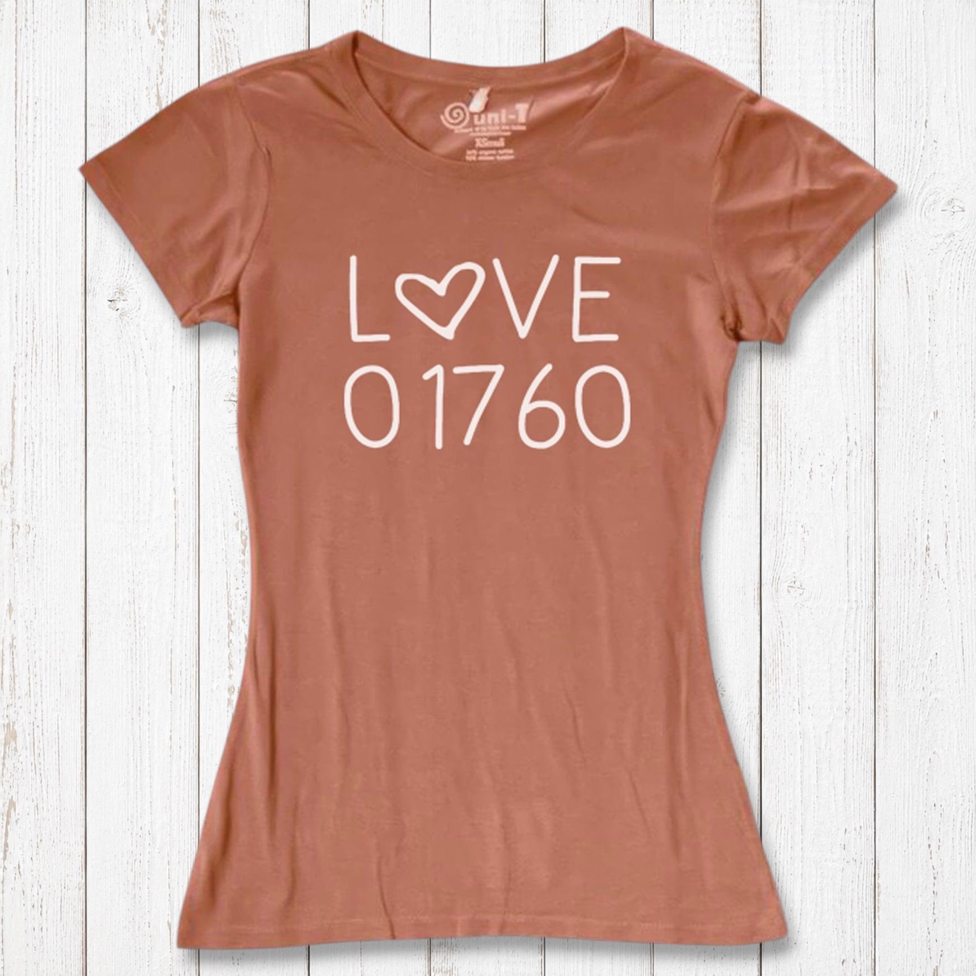 Rust-colored women's graphic T-shirt with 'LOVE 01760' text and heart design, made of organic cotton and bamboo, laid on white wooden background