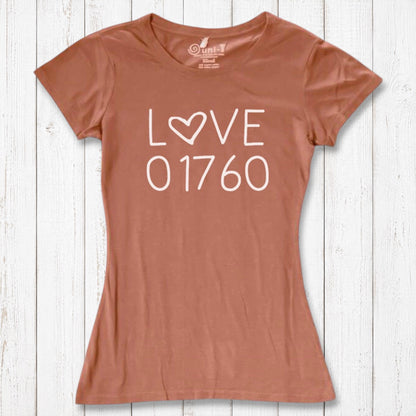 Rust-colored women's graphic T-shirt with 'LOVE 01760' text and heart design, made of organic cotton and bamboo, laid on white wooden background