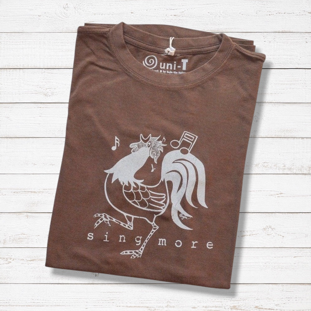 Folded brown 'Sing More' rooster t-shirt for men made from bamboo and organic cotton, featuring a funny farm animal graphic.