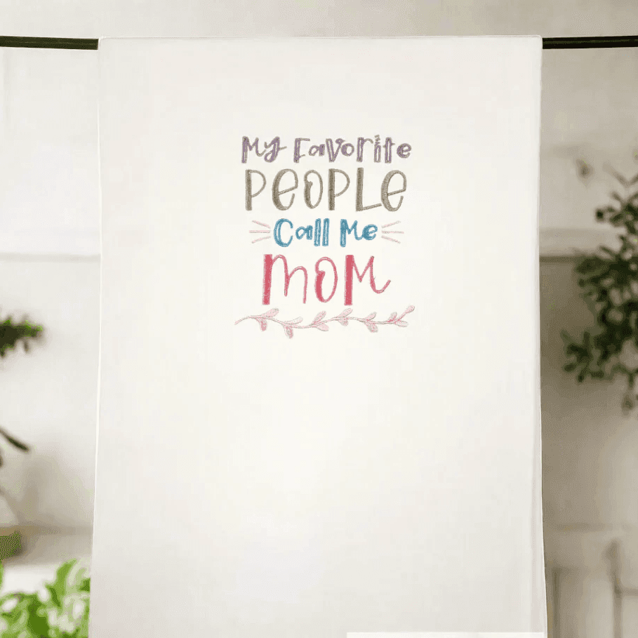 Heartwarming embroidered kitchen towel hanging on display with 'My favorite people call me Mom' design. Perfect Mother's Day or home gift.
