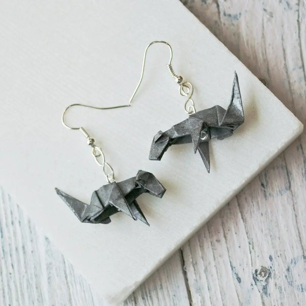 Pair of grey origami dog earrings displayed on a white surface, highlighting their handcrafted paper design and modern aesthetic.