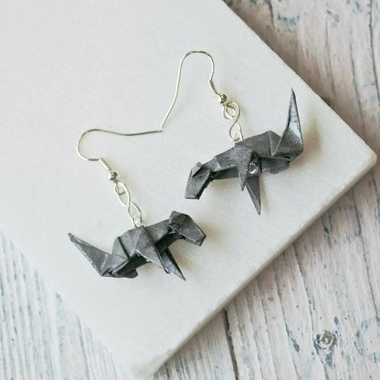 Pair of grey origami dog earrings displayed on a white surface, highlighting their handcrafted paper design and modern aesthetic.