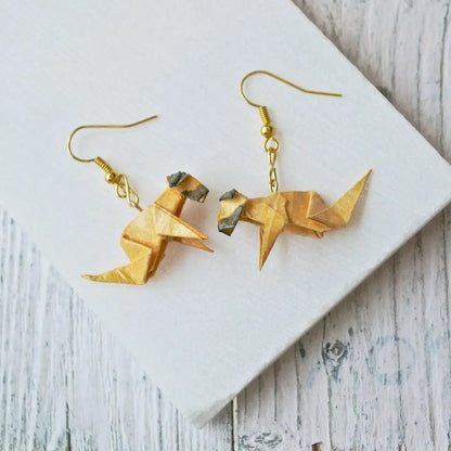Flat lay of Origami Dog Paper Earrings on white wood, highlighting the detailed craftsmanship and artistic style in tan and brown tones.