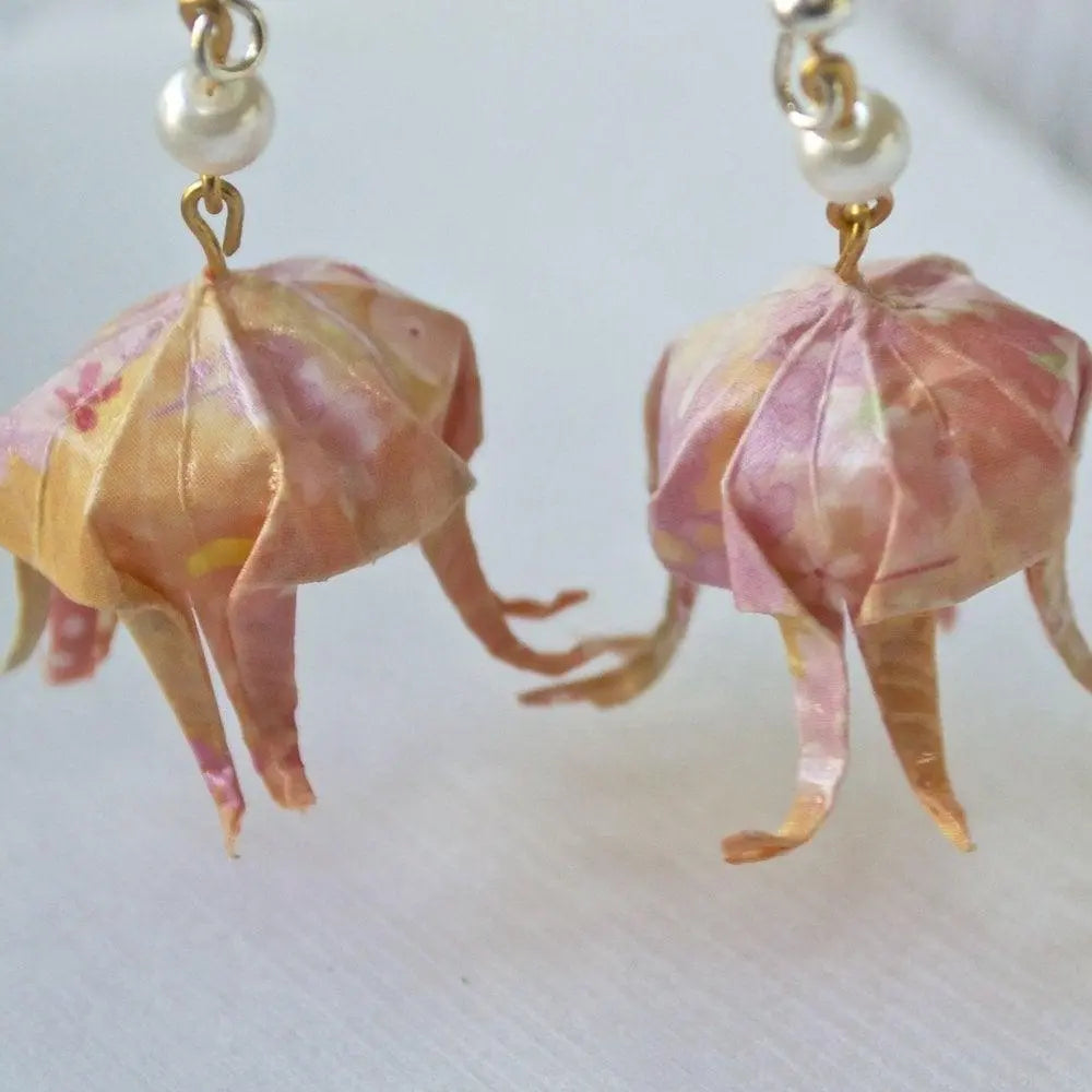 Close-up of unique origami jellyfish earrings showing intricate paper folds and delicate tentacle details in soft pink and peach hues.
