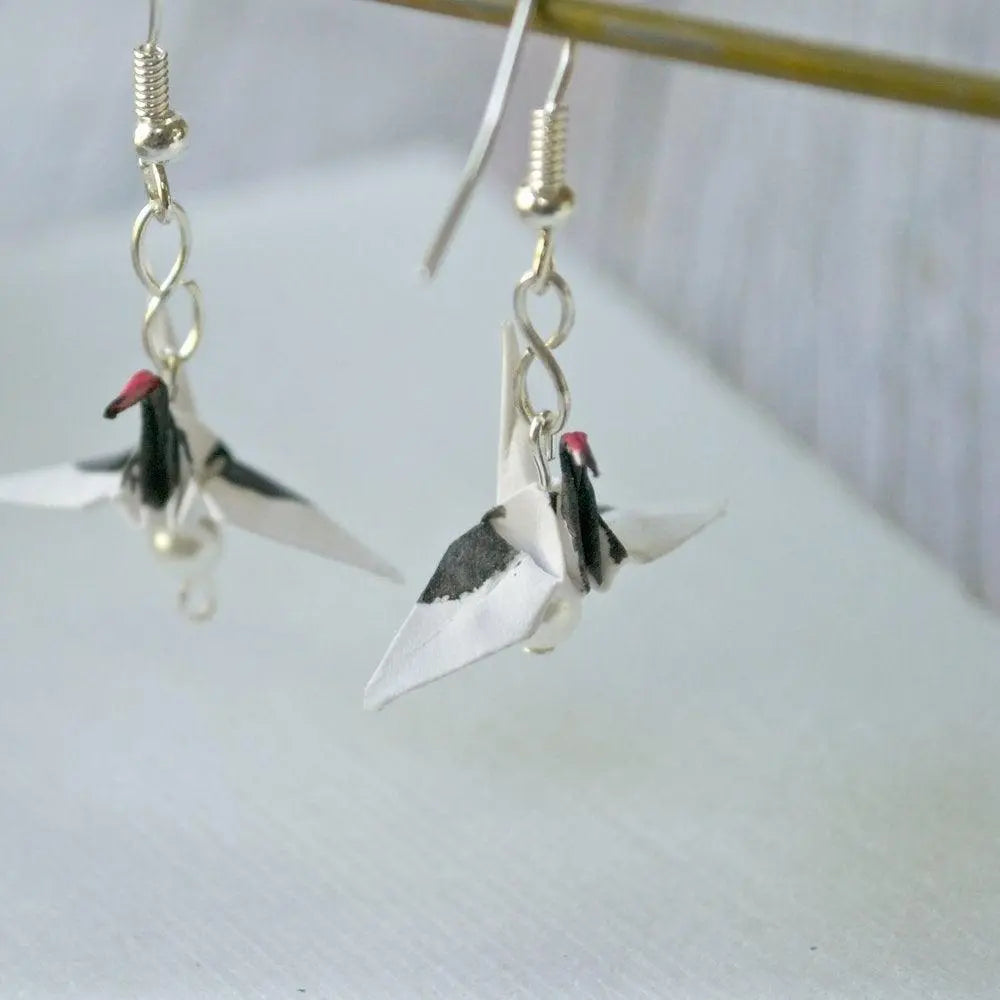 Unique origami crane earrings with red crested design, handcrafted from paper and suspended on silver hooks for a lightweight accessory.