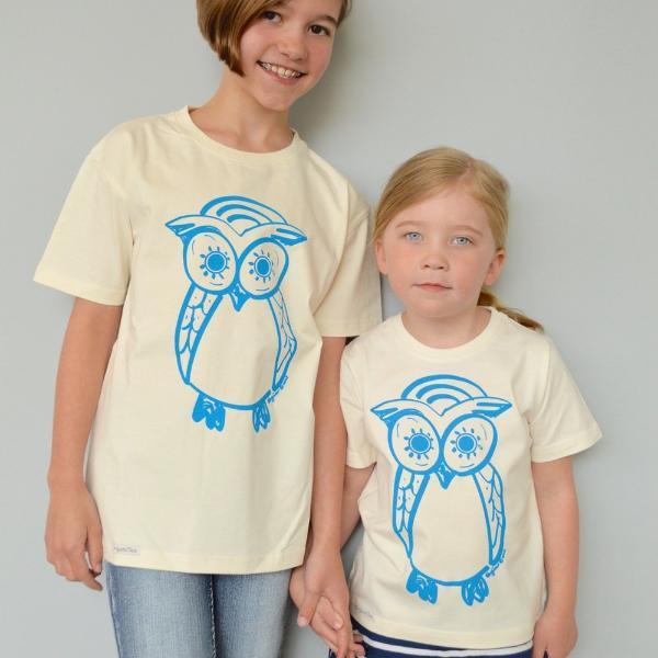 Two children wearing cream Kids' Organic Cotton Owl T-Shirts with blue owl print. Uni-T eco-friendly matching wildlife tops for siblings.