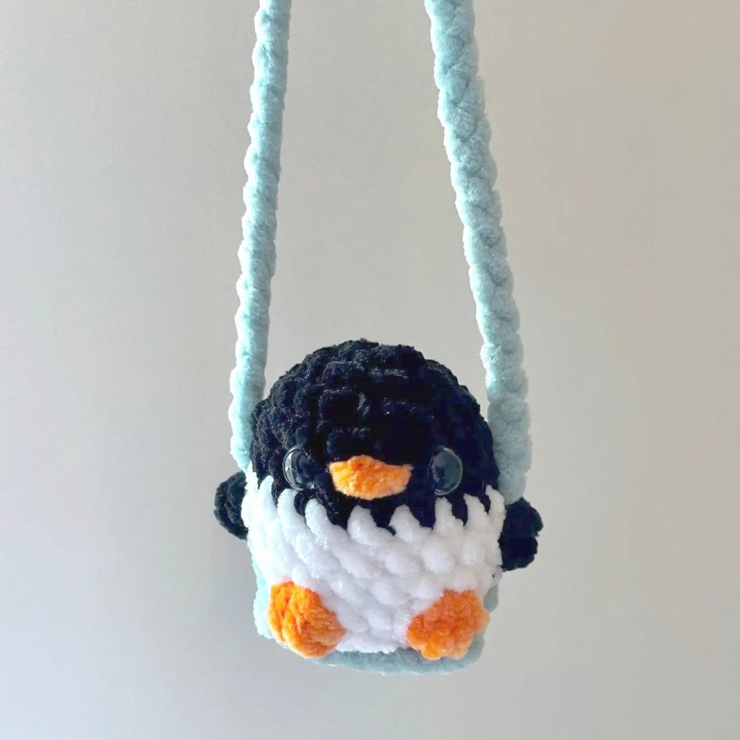 Penguin Car Mirror Swing - Fun Accessory featuring a handmade plush penguin with orange feet and beak, hanging from a soft blue chenille yarn loop. Ideal small gift for car decor and stress relief.