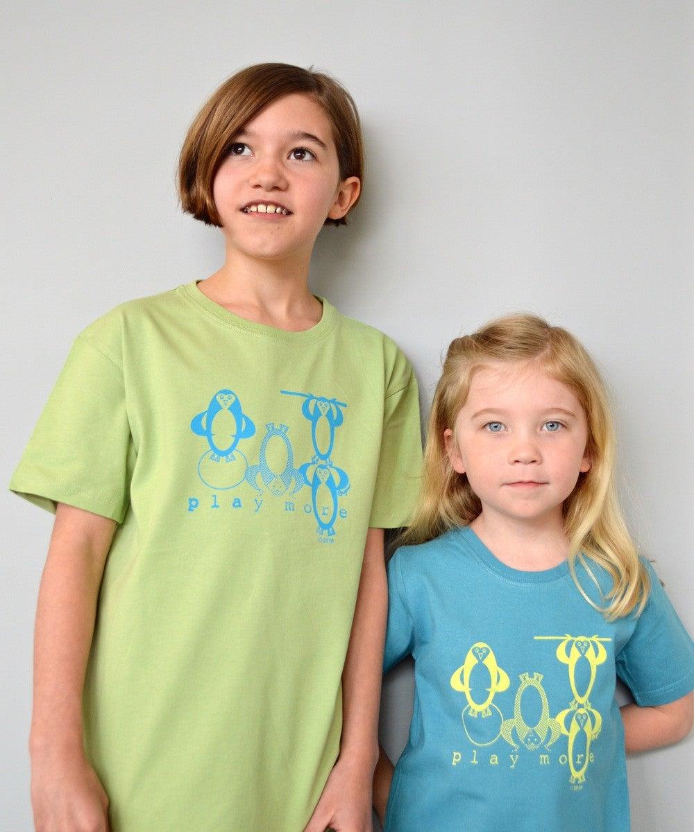 Two children wearing Kids' Penguin Organic Cotton T-Shirts in green and blue, featuring playful sea life penguins and 'play more' slogan.