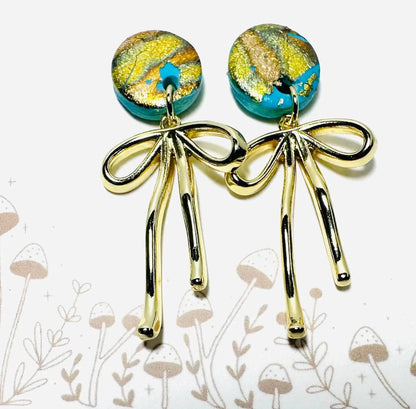 Round turquoise polymer clay earrings with gold foil and dangling gold bow charms, a whimsical and affordable gift option.